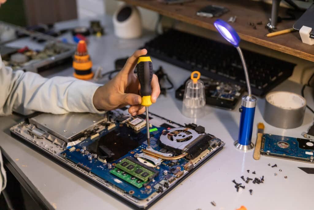 Technician using a screwdriver inside an open laptop on a repair bench
